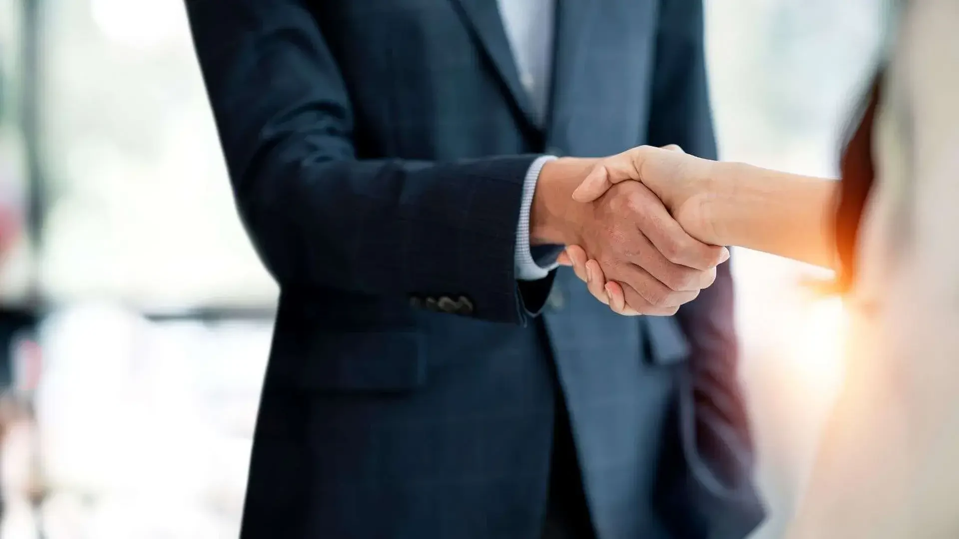 Two people shaking hands, one wearing a dark suit, signifying a business agreement or partnership.